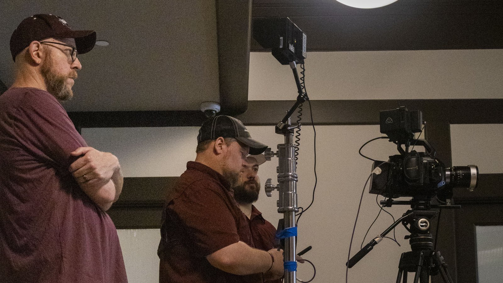 Marty Lang watches a video shoot as two crew members set up lighting and camera equipment.